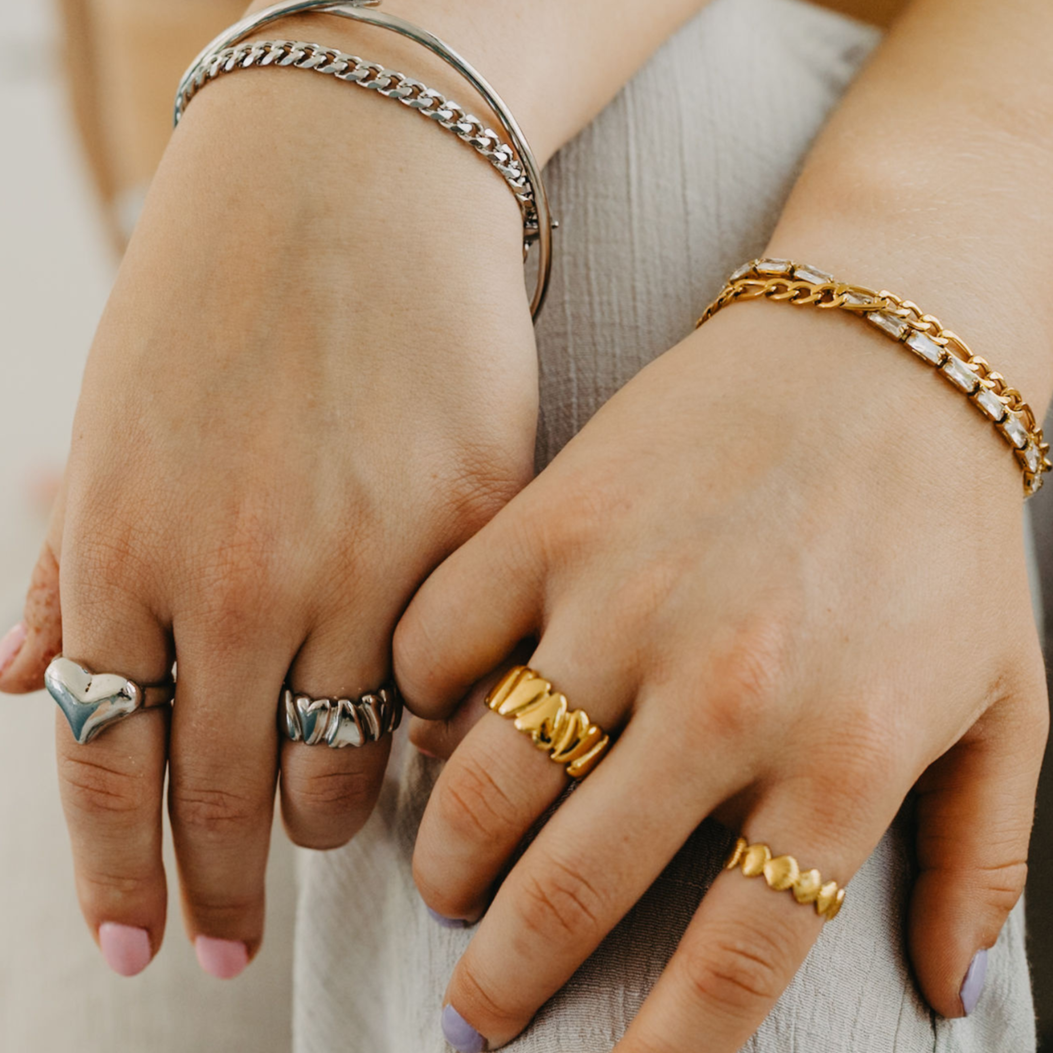 Close-up of women’s hands wearing adjustable waterproof silver heart ring with stacked rings and bracelets at pool