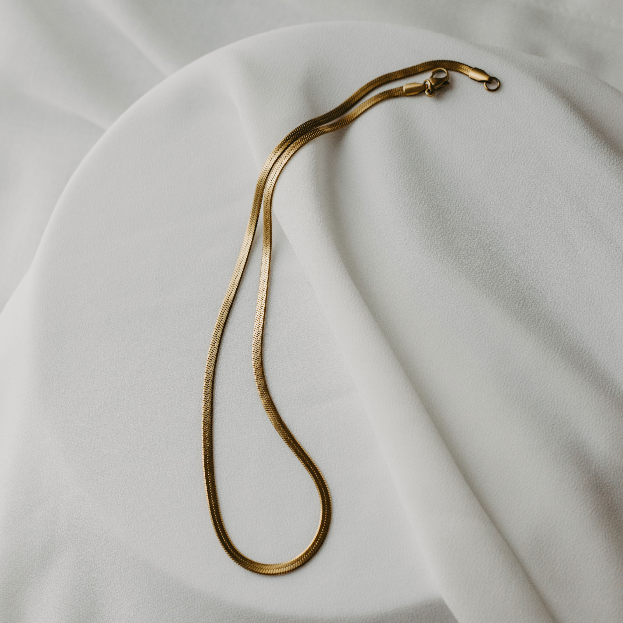 Eclipse herringbone necklace in 18K gold PVD displayed on white texture waterproof gold jewelry