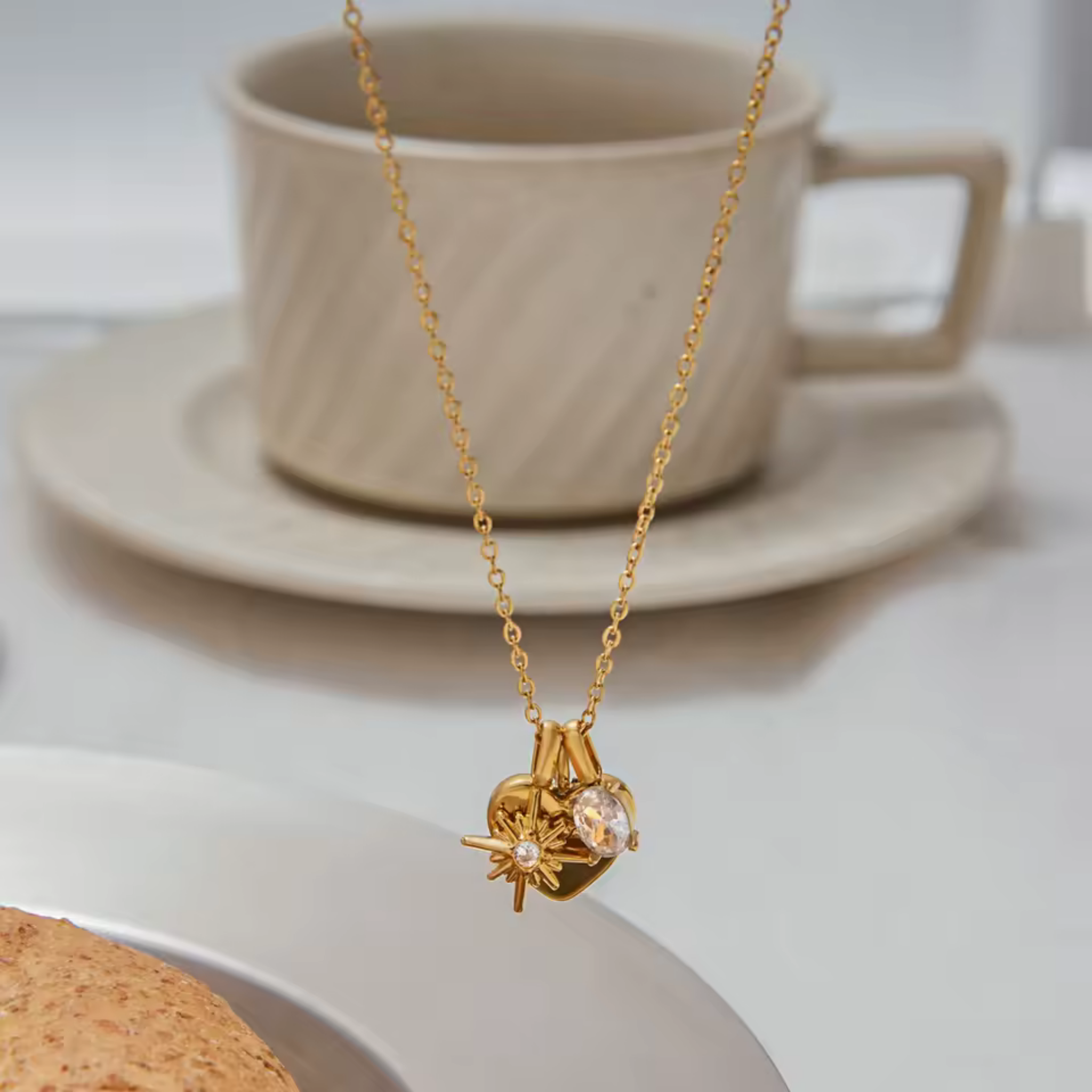 gold Mom Moments heart charm necklace styled on table with coffee cup, featuring engraved mom heart, starburst charm, and oval cubic zirconia pendant
