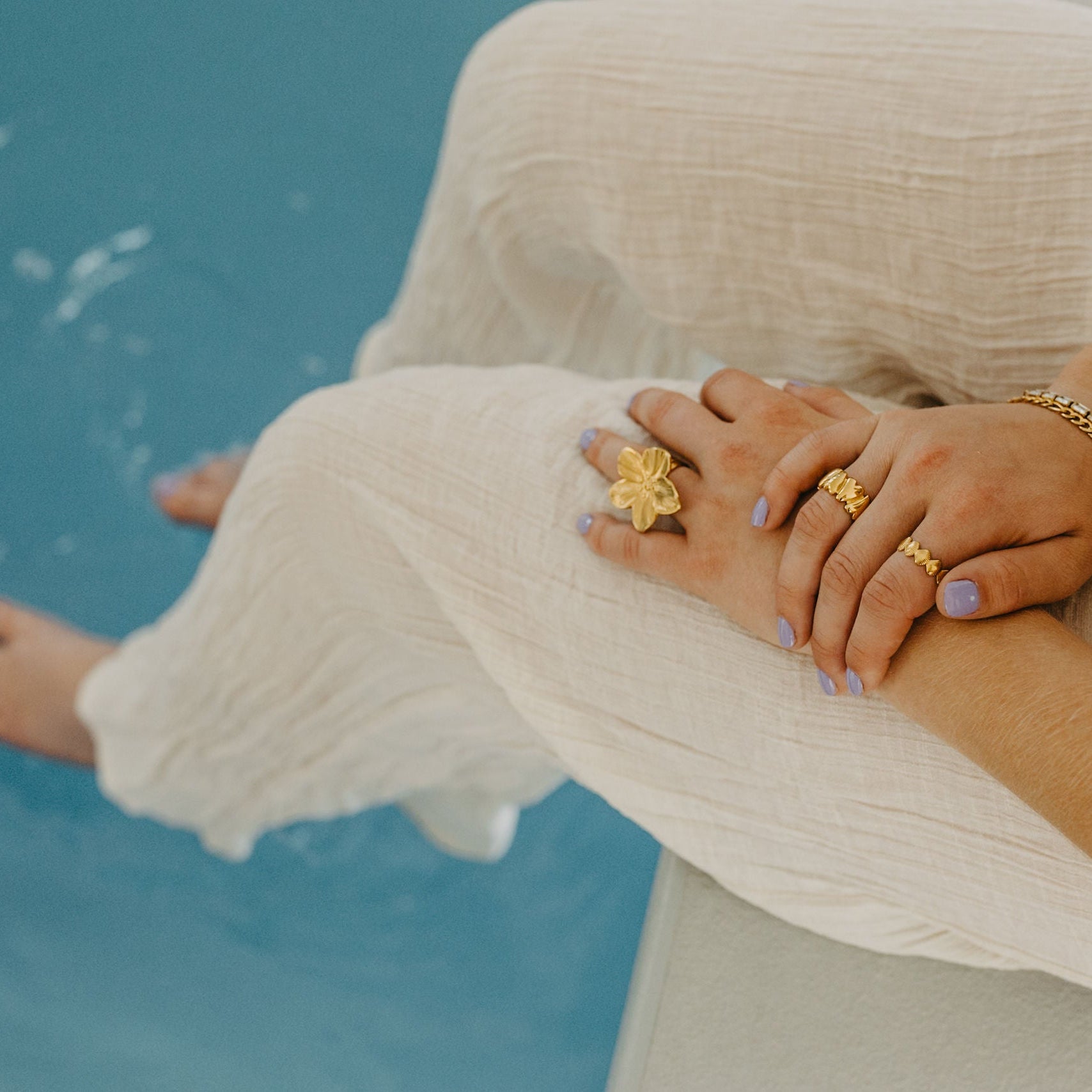 Close-up of women’s hands wearing adjustable waterproof silver heart ring with stacked rings and bracelets at pool