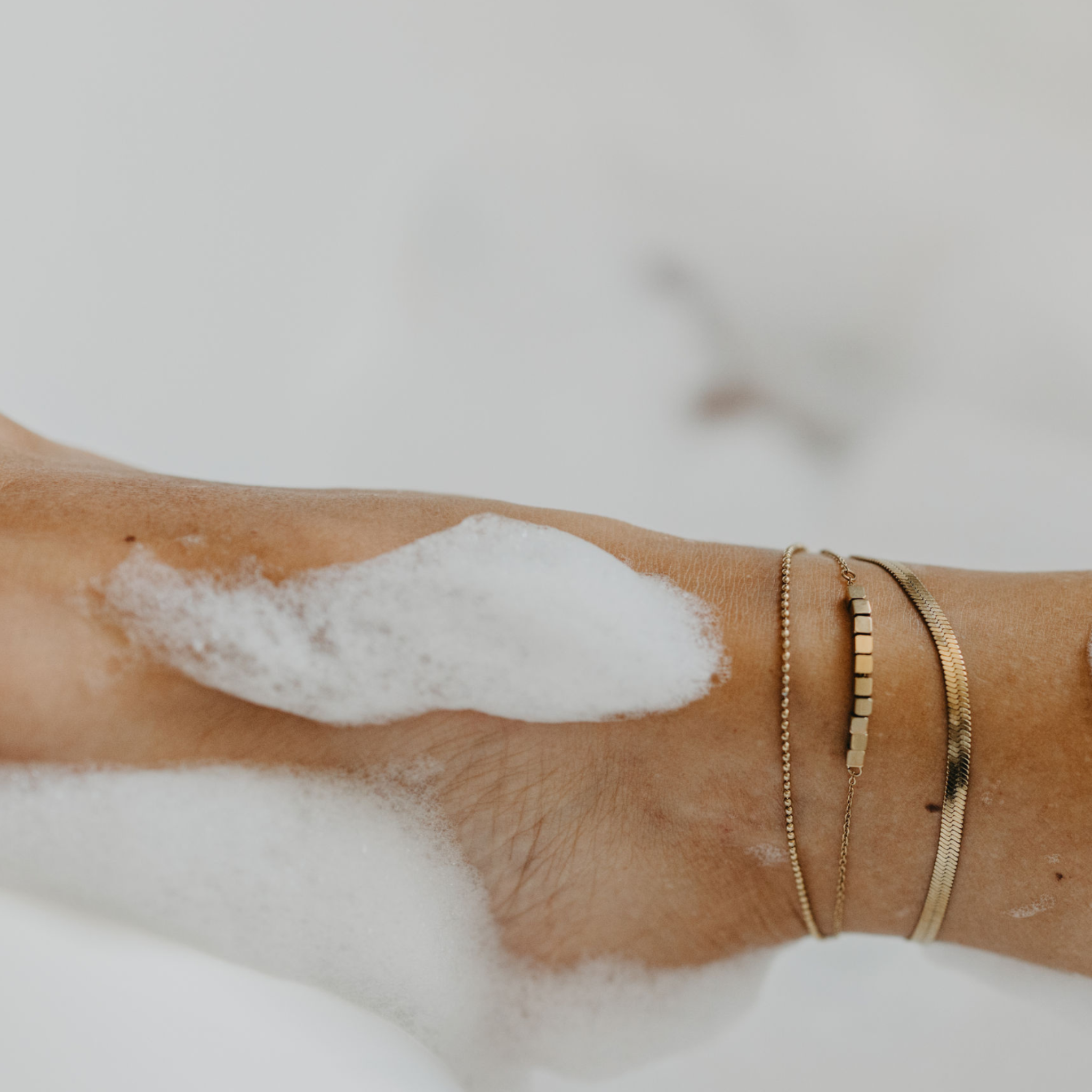 Close up details of a model wearing the Aphrodite Waterproof Gold Layered Anklet paired with the Eclipse Waterproof Gold Herringbone Anklet.