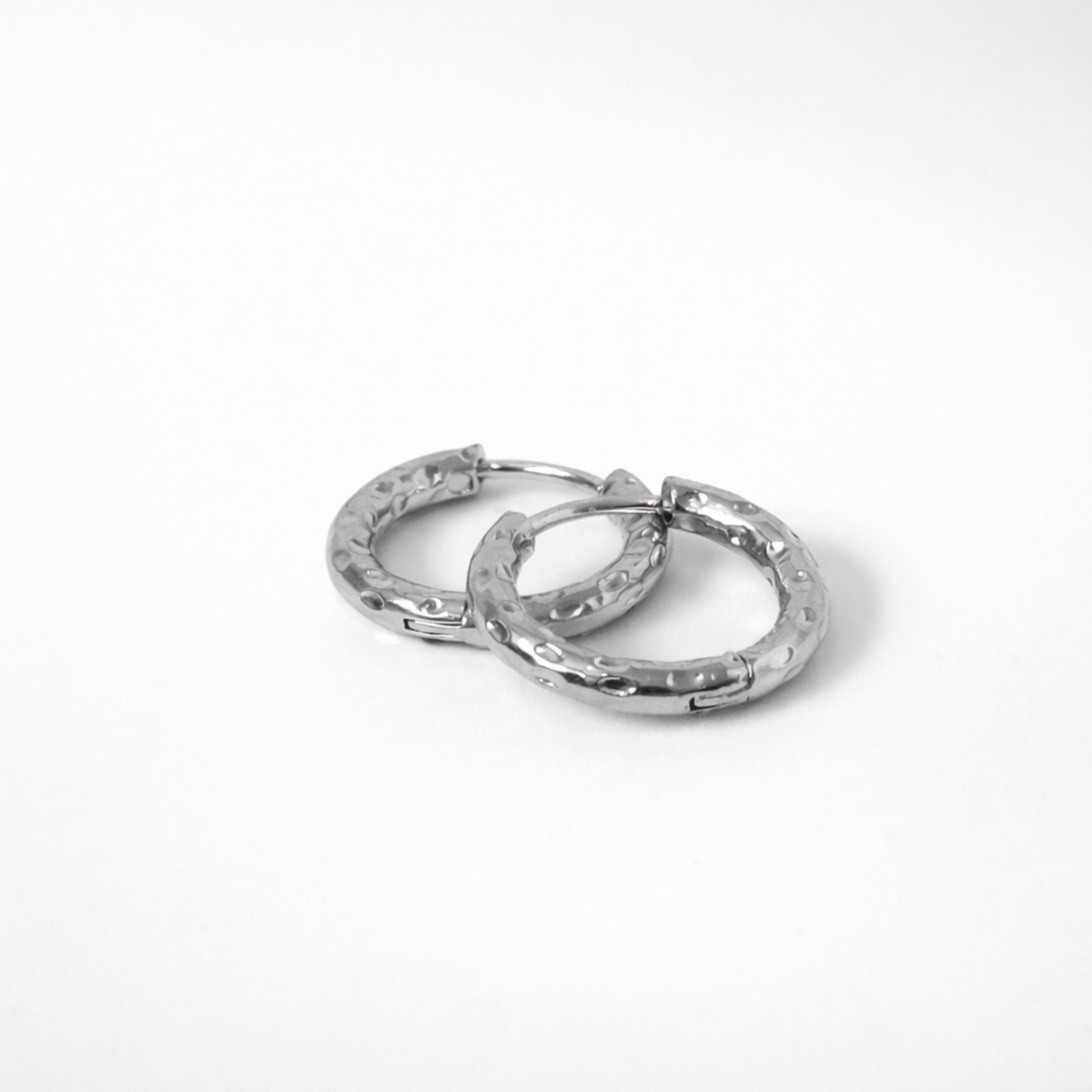 Aura hoop earrings in silver stainless steel with hammered texture in huggie style on white background