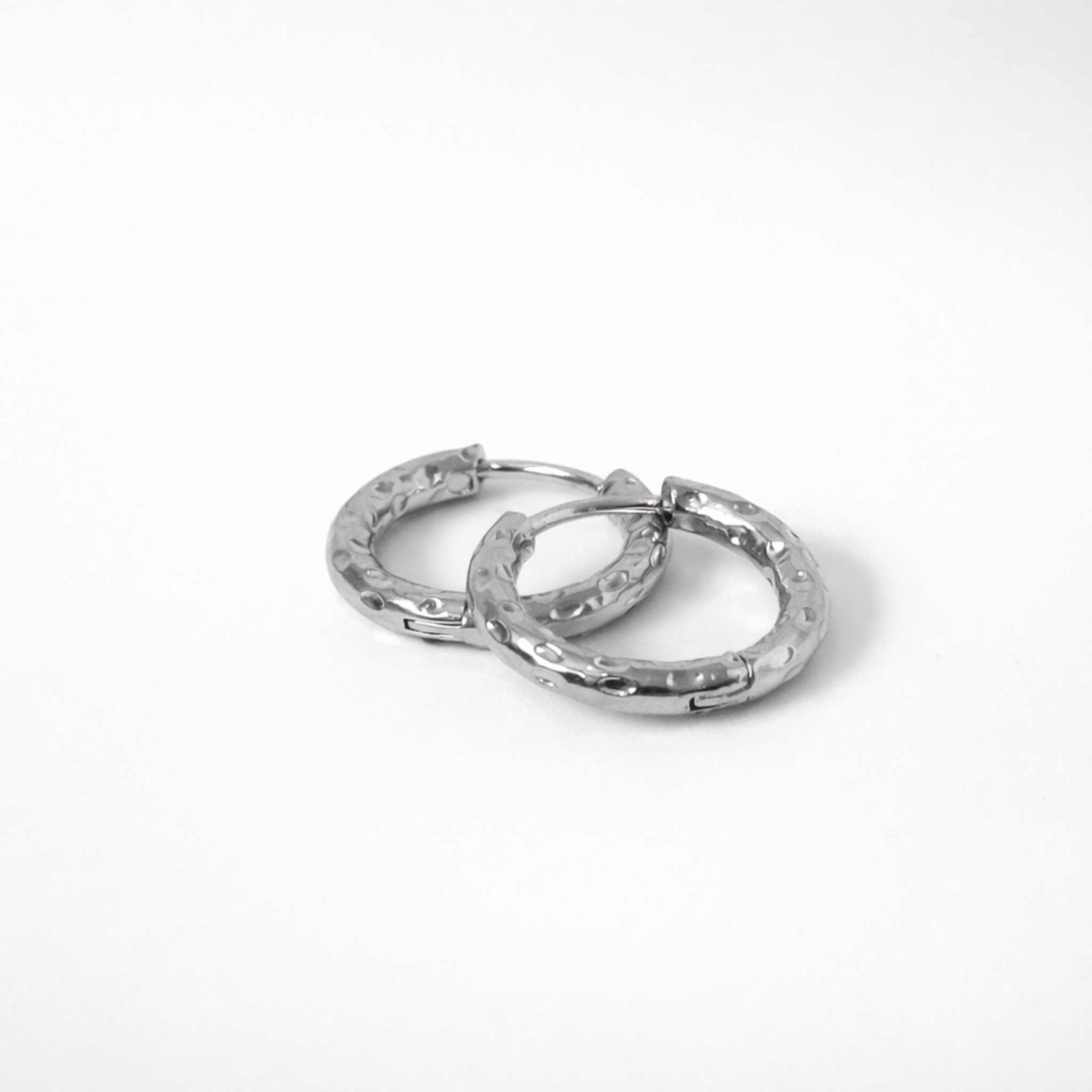 Aura hoop earrings in silver stainless steel with hammered texture in huggie style on white background