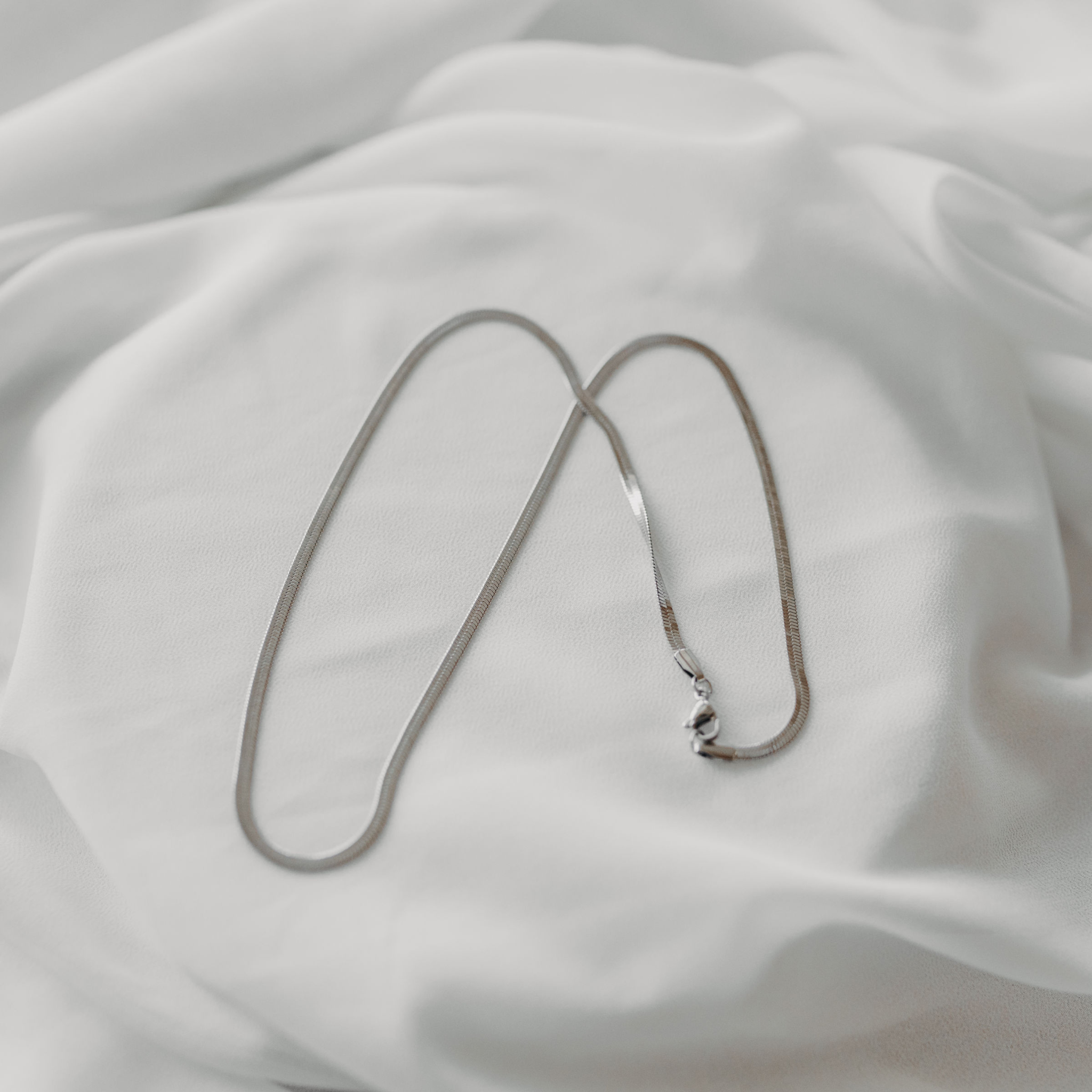 Eclipse herringbone necklace in silver stainless steel displayed on soft white fabric waterproof jewelry