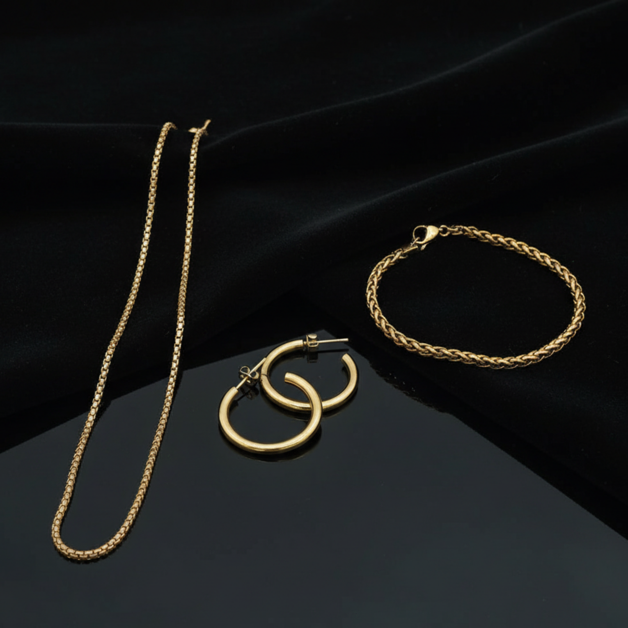 Essential Set jewelry featuring 18K gold PVD waterproof necklace, bracelet and hoop earrings displayed on black background, tarnish resistant gold jewelry set