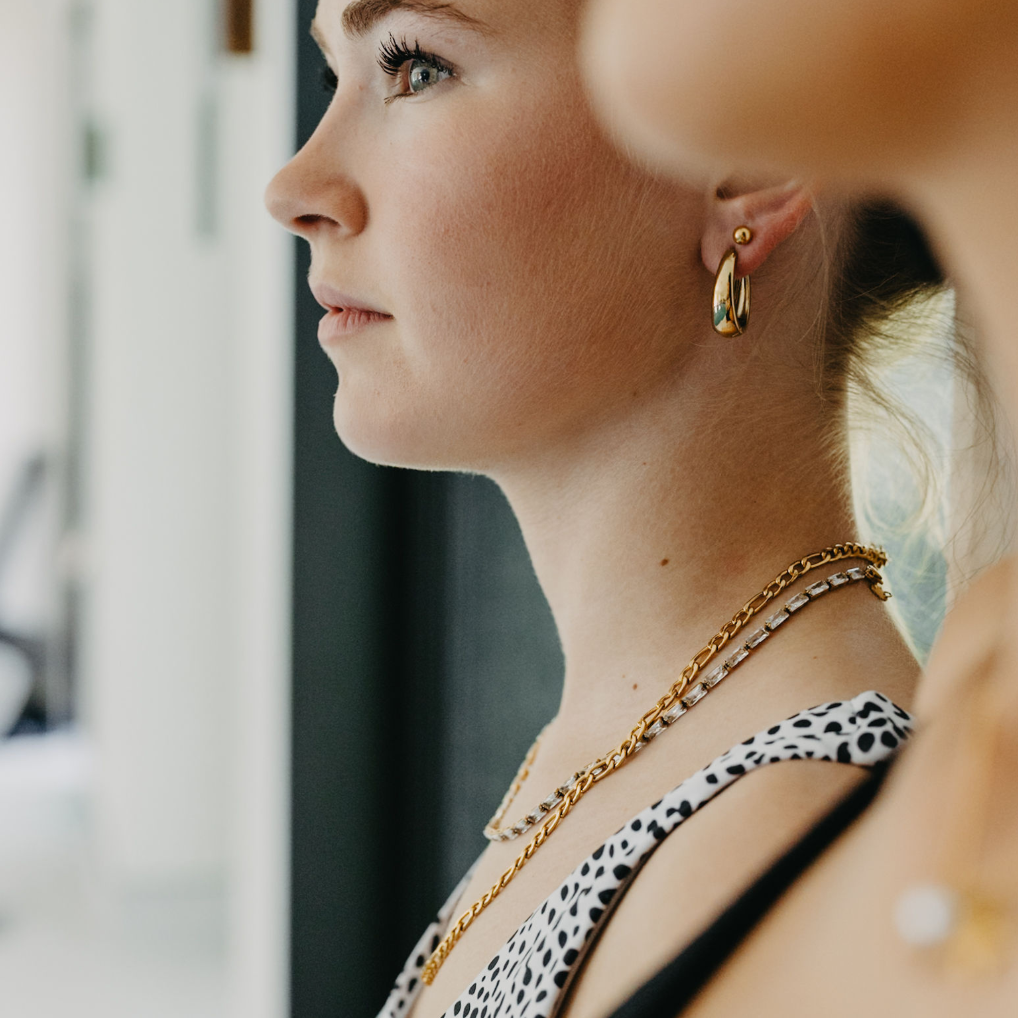 model wearing Forge figaro chain necklace layered with gold waterproof jewelry and gold hoop earrings