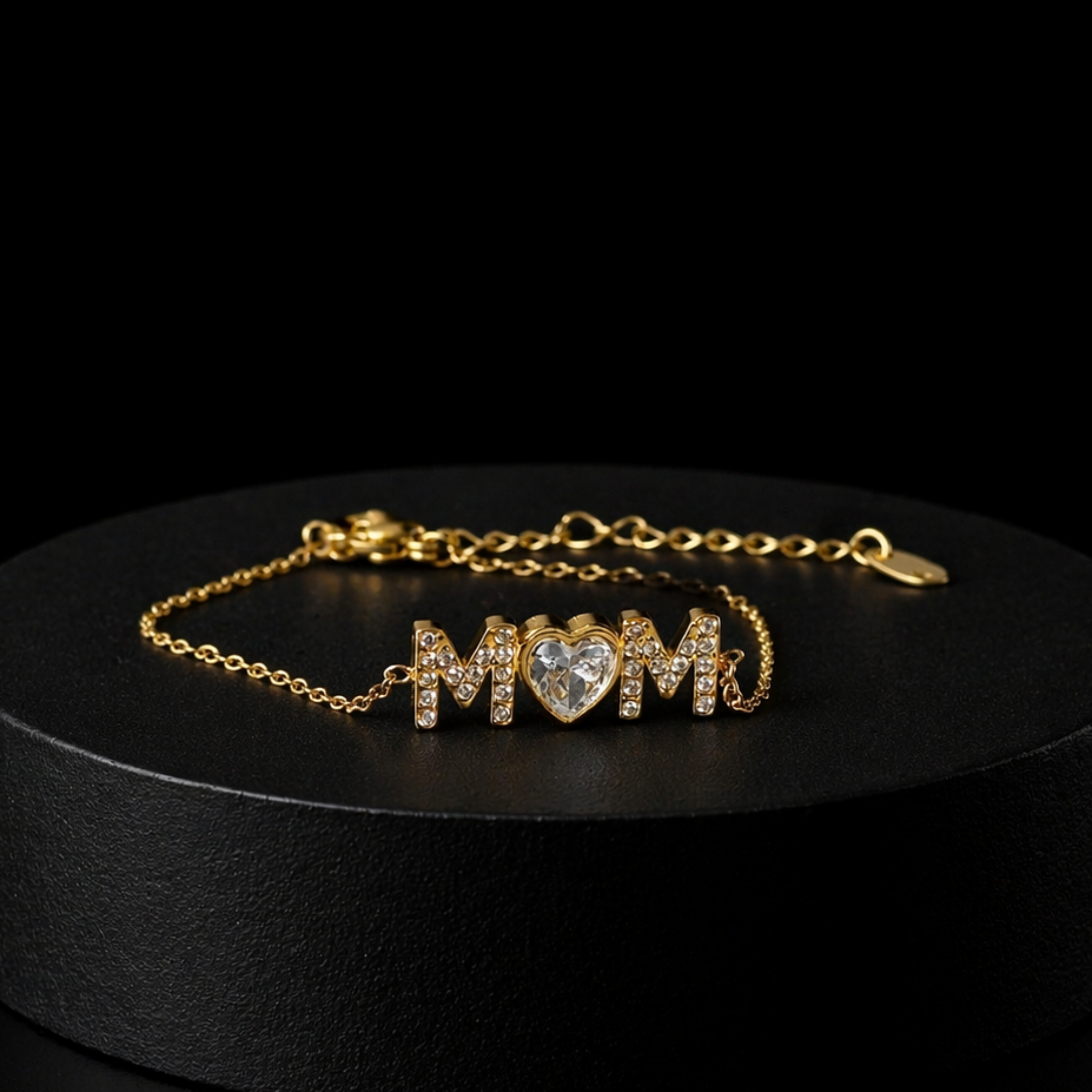 Mom Radiance bracelet displayed on black pedestal featuring gold MOM letters with cubic zirconia and heart center stone